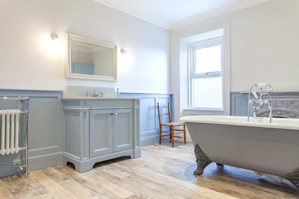 Immagine di una stanza da bagno tradizionale con ante blu, vasca con piedi a zampa di leone, vasca/doccia, pareti blu e top in legno