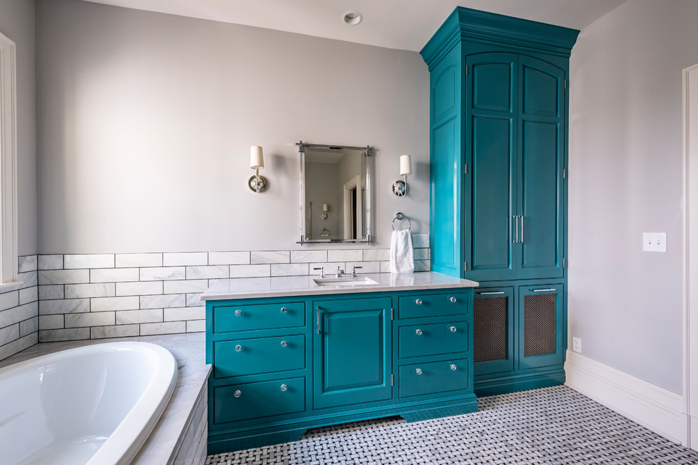 Exemple d'une salle de bain principale chic de taille moyenne avec un placard avec porte à panneau surélevé, des portes de placard bleues, une baignoire posée, un carrelage gris, du carrelage en marbre, un mur gris, un sol en marbre, un lavabo encastré, un plan de toilette en marbre, un sol gris et un plan de toilette gris.