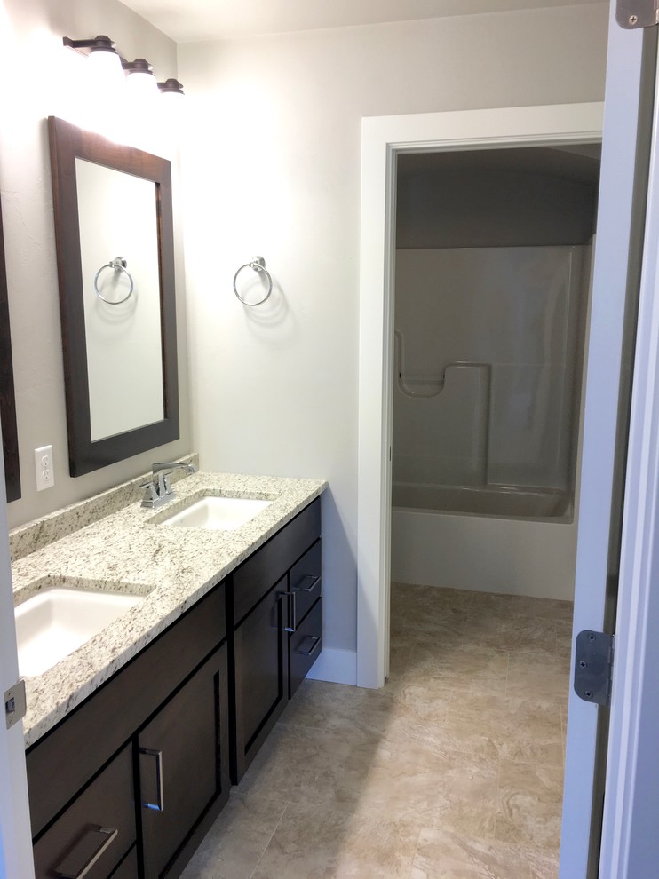 Bild på ett amerikanskt badrum, med luckor med infälld panel, skåp i mörkt trä, ett platsbyggt badkar, en dusch/badkar-kombination, flerfärgad kakel, keramikplattor, grå väggar, klinkergolv i keramik, ett integrerad handfat och granitbänkskiva