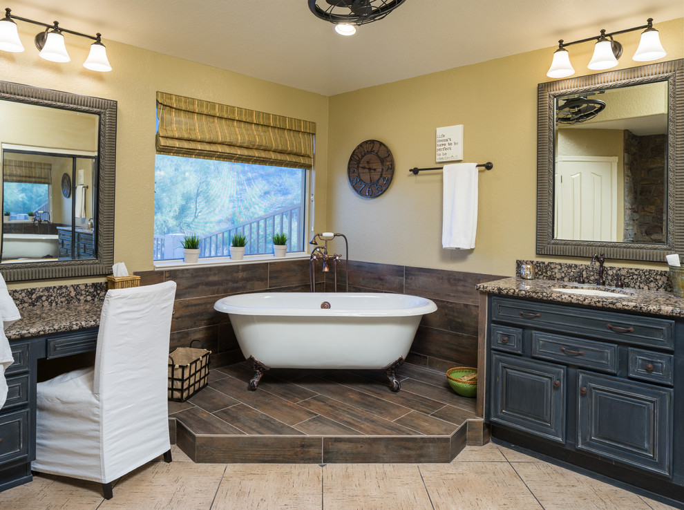 Foto på ett vintage en-suite badrum, med luckor med upphöjd panel, skåp i slitet trä, ett badkar med tassar, gula väggar, ett undermonterad handfat och granitbänkskiva