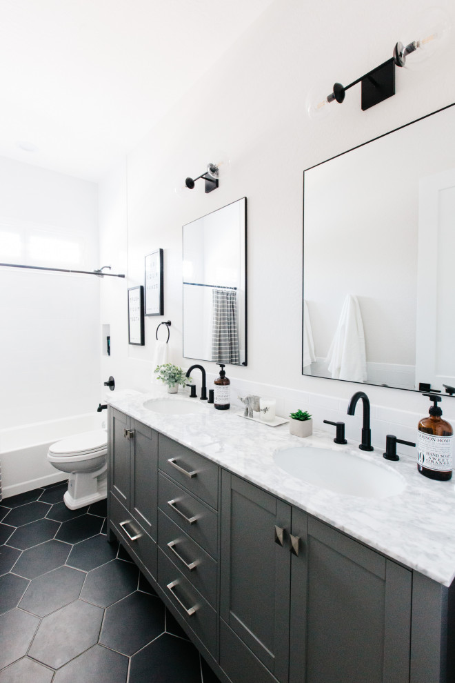 Idée de décoration pour une salle de bain tradition avec un placard à porte shaker, des portes de placard grises, une baignoire en alcôve, un mur blanc, un lavabo encastré, un sol noir, un plan de toilette blanc et meuble double vasque.