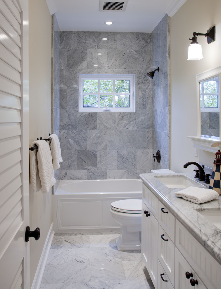 Modelo de cuarto de baño gris y blanco marinero con puertas de armario blancas, bañera empotrada, combinación de ducha y bañera, baldosas y/o azulejos grises y encimeras grises