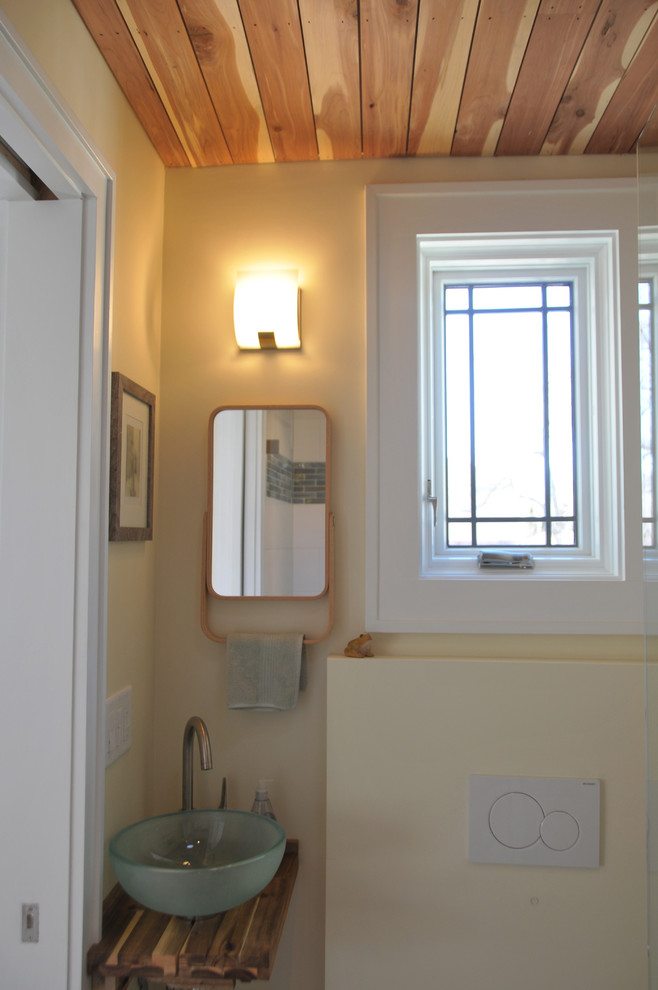 Bild på ett litet funkis badrum, med en dusch i en alkov, en vägghängd toalettstol, vit kakel, gula väggar och ett fristående handfat