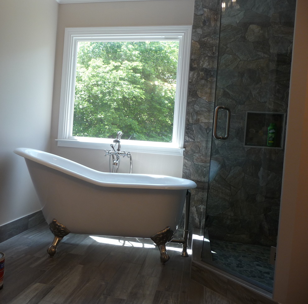 Klassisk inredning av ett mellanstort badrum, med ett badkar med tassar, en hörndusch, grå kakel, stenkakel, beige väggar, mellanmörkt trägolv, granitbänkskiva, brunt golv och dusch med gångjärnsdörr