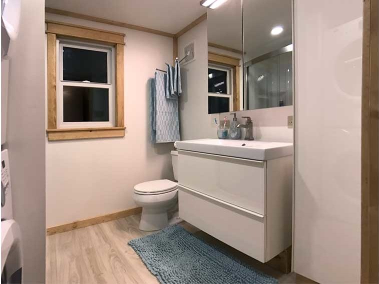 Bild på ett litet funkis en-suite badrum, med släta luckor, vita skåp, en dusch i en alkov, en toalettstol med separat cisternkåpa, beige väggar, laminatgolv, ett konsol handfat och bänkskiva i akrylsten
