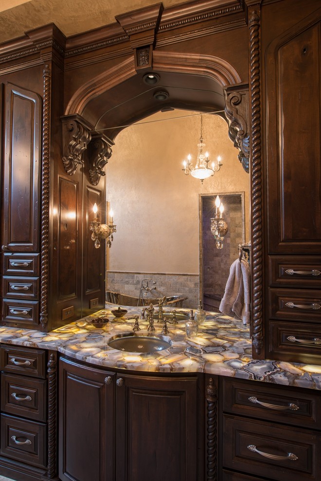 Photo of a large mediterranean ensuite bathroom in Austin with a submerged sink, recessed-panel cabinets, dark wood cabinets, a freestanding bath, grey tiles and beige walls.
