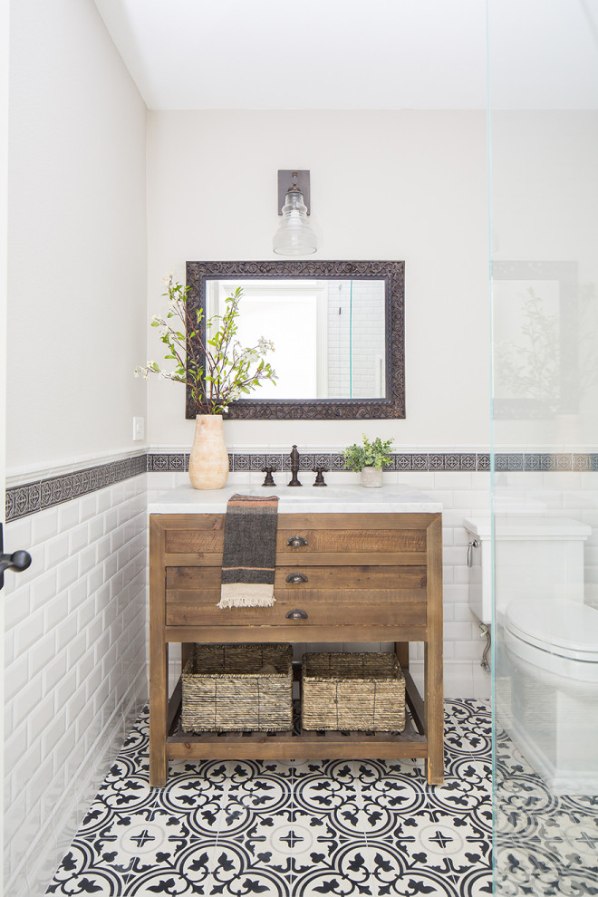 Стильный дизайн: маленькая ванная комната в стиле кантри с фасадами цвета дерева среднего тона, угловым душем, унитазом-моноблоком, черно-белой плиткой, керамической плиткой, бежевыми стенами, полом из цементной плитки, душевой кабиной, врезной раковиной, мраморной столешницей, разноцветным полом, душем с распашными дверями, белой столешницей, тумбой под одну раковину, напольной тумбой и плоскими фасадами для на участке и в саду - последний тренд
