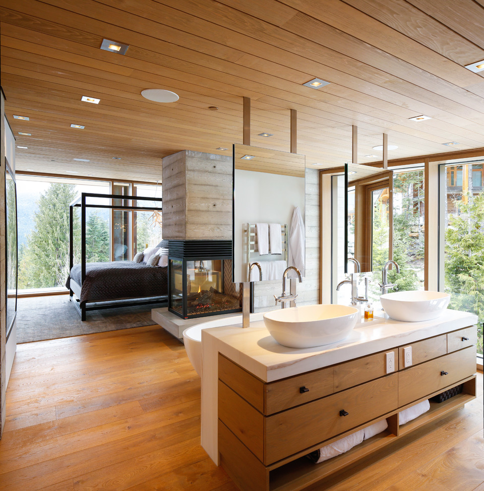 Cette photo montre une grande salle de bain principale montagne en bois clair avec un placard à porte plane, une baignoire indépendante, une vasque, un plan de toilette en surface solide, un sol en bois brun et un sol beige.