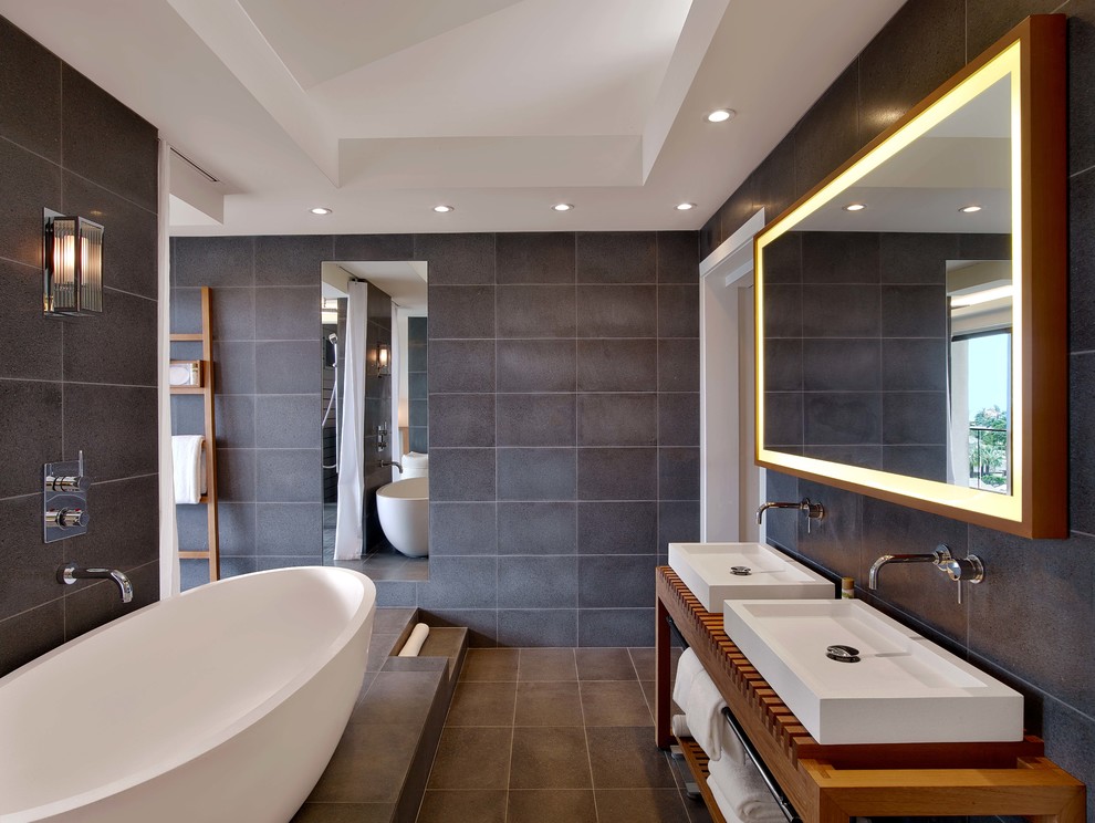 На фото: большая главная ванная комната в современном стиле с отдельно стоящей ванной, открытым душем, настольной раковиной, столешницей из дерева, серой плиткой, каменной плиткой, серыми стенами, открытыми фасадами и фасадами цвета дерева среднего тона