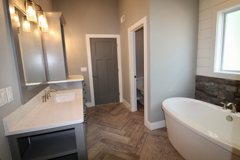 Réalisation d'une salle de bain principale craftsman de taille moyenne avec un placard à porte shaker, des portes de placard grises, une baignoire indépendante, un espace douche bain, WC séparés, un carrelage blanc, des carreaux de porcelaine, un mur gris, un sol en carrelage de céramique, un lavabo encastré, un plan de toilette en quartz modifié, un sol gris et une cabine de douche à porte battante.