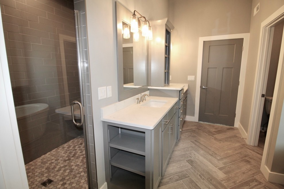 Exemple d'une salle de bain principale craftsman de taille moyenne avec un placard à porte shaker, des portes de placard grises, une baignoire indépendante, un espace douche bain, WC séparés, un carrelage blanc, des carreaux de porcelaine, un mur gris, un sol en carrelage de céramique, un lavabo encastré, un plan de toilette en quartz modifié, un sol gris et une cabine de douche à porte battante.