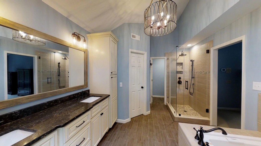 Large traditional ensuite bathroom in Raleigh with raised-panel cabinets, beige cabinets, a built-in bath, a corner shower, a two-piece toilet, brown tiles, ceramic tiles, blue walls, porcelain flooring, a submerged sink, engineered stone worktops, brown floors, a hinged door and black worktops.