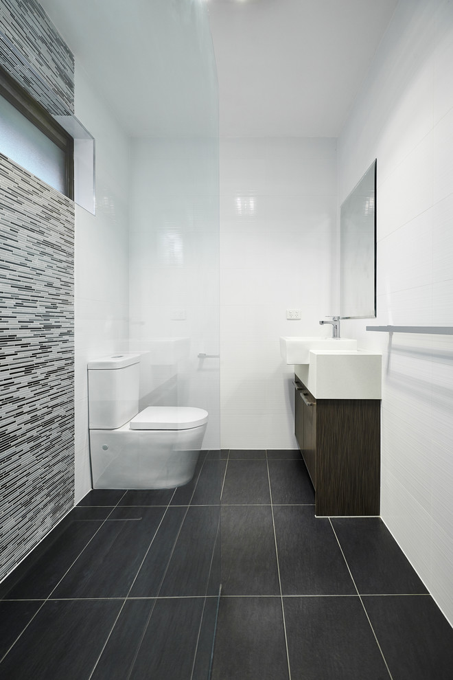 Пример оригинального дизайна: ванная комната в стиле модернизм с настольной раковиной, плоскими фасадами, темными деревянными фасадами, серой плиткой, удлиненной плиткой, белыми стенами и черным полом