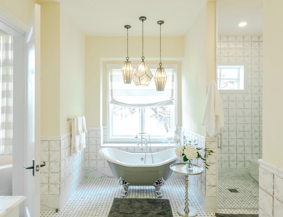 Bild på ett stort lantligt badrum, med ett badkar med tassar, grå kakel, vit kakel, gula väggar, vitt golv, en dusch i en alkov, marmorgolv, ett fristående handfat, bänkskiva i täljsten och dusch med gångjärnsdörr