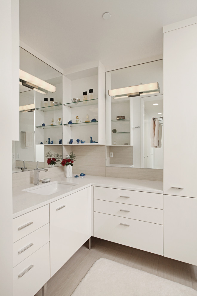 Bild på ett funkis vit vitt badrum, med ett undermonterad handfat, en dusch i en alkov, en toalettstol med hel cisternkåpa, släta luckor, vita skåp, bänkskiva i kvartsit och beige kakel