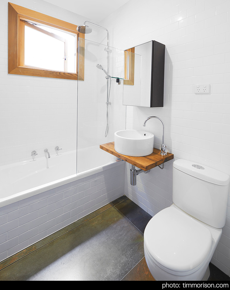 Modelo de cuarto de baño contemporáneo con armarios tipo vitrina, encimera de madera, sanitario de dos piezas, baldosas y/o azulejos blancos y suelo de baldosas de cerámica