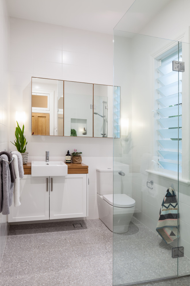 Inspiration for a small contemporary bathroom in Sydney with shaker cabinets, white cabinets, a corner shower, a one-piece toilet, white tiles, porcelain tiles, white walls, porcelain flooring, a built-in sink, wooden worktops, grey floors, a hinged door, brown worktops, a wall niche, a single sink and a floating vanity unit.