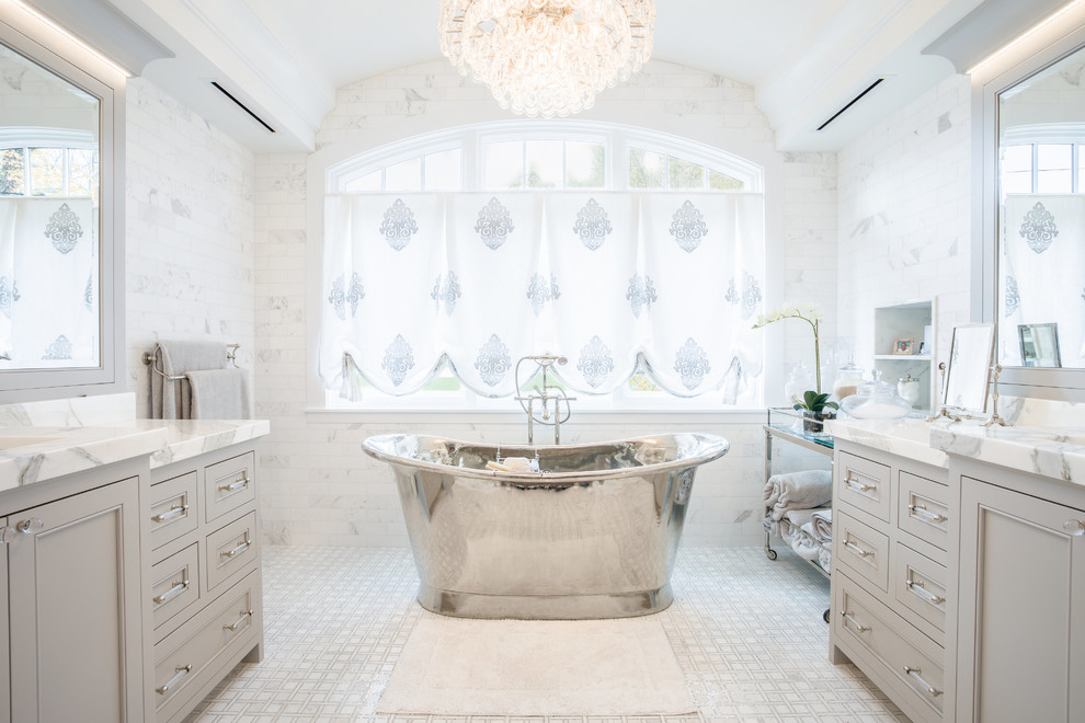 Пример оригинального дизайна: огромная главная ванная комната в стиле неоклассика (современная классика) с фасадами с утопленной филенкой, серыми фасадами, мраморной столешницей, отдельно стоящей ванной, белой плиткой и белым полом