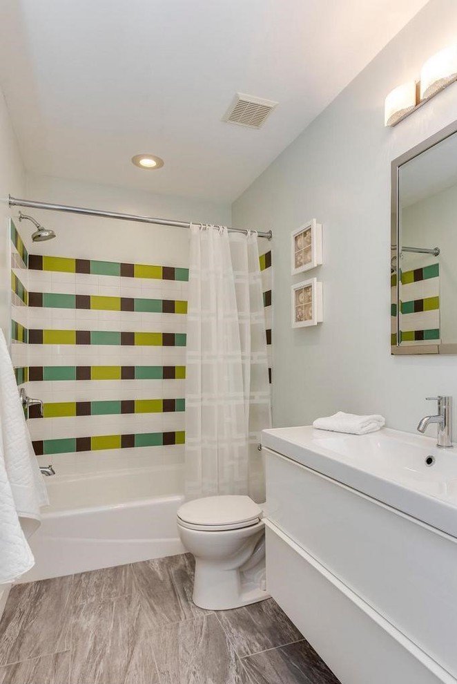 Inredning av ett litet vit vitt badrum för barn, med släta luckor, vita skåp, ett badkar i en alkov, en dusch/badkar-kombination, en toalettstol med separat cisternkåpa, flerfärgad kakel, keramikplattor, grå väggar, klinkergolv i keramik, ett väggmonterat handfat, bänkskiva i glas, grått golv och dusch med duschdraperi