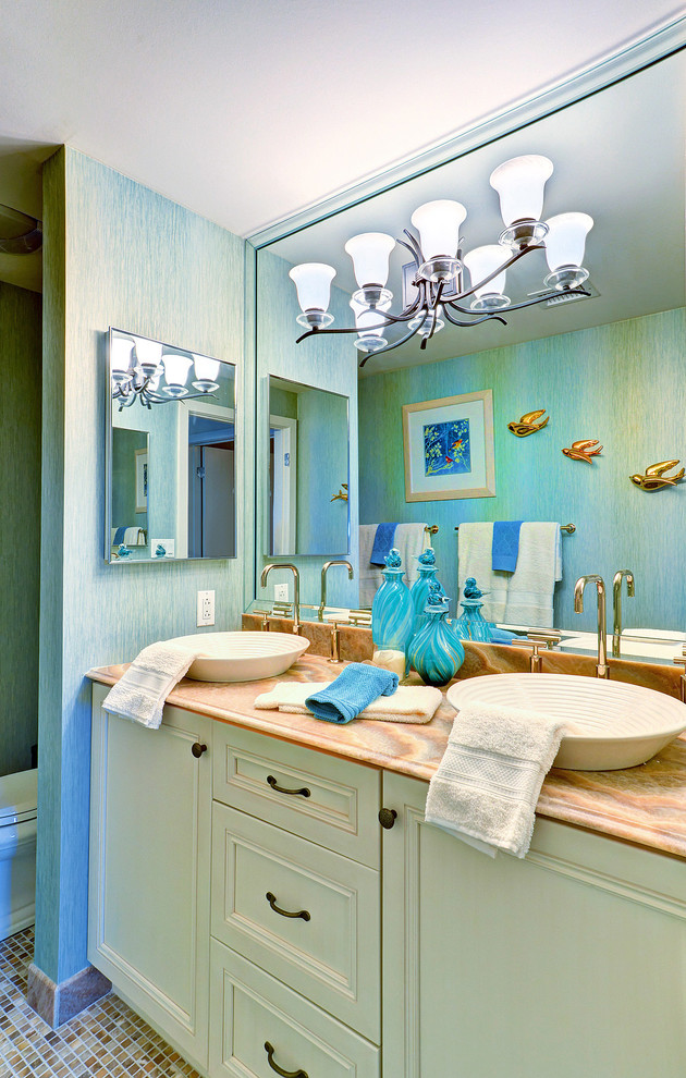 Diseño de cuarto de baño principal costero de tamaño medio con lavabo sobreencimera, armarios con paneles empotrados, puertas de armario blancas, encimera de ónix, ducha empotrada, baldosas y/o azulejos beige, paredes azules y suelo con mosaicos de baldosas