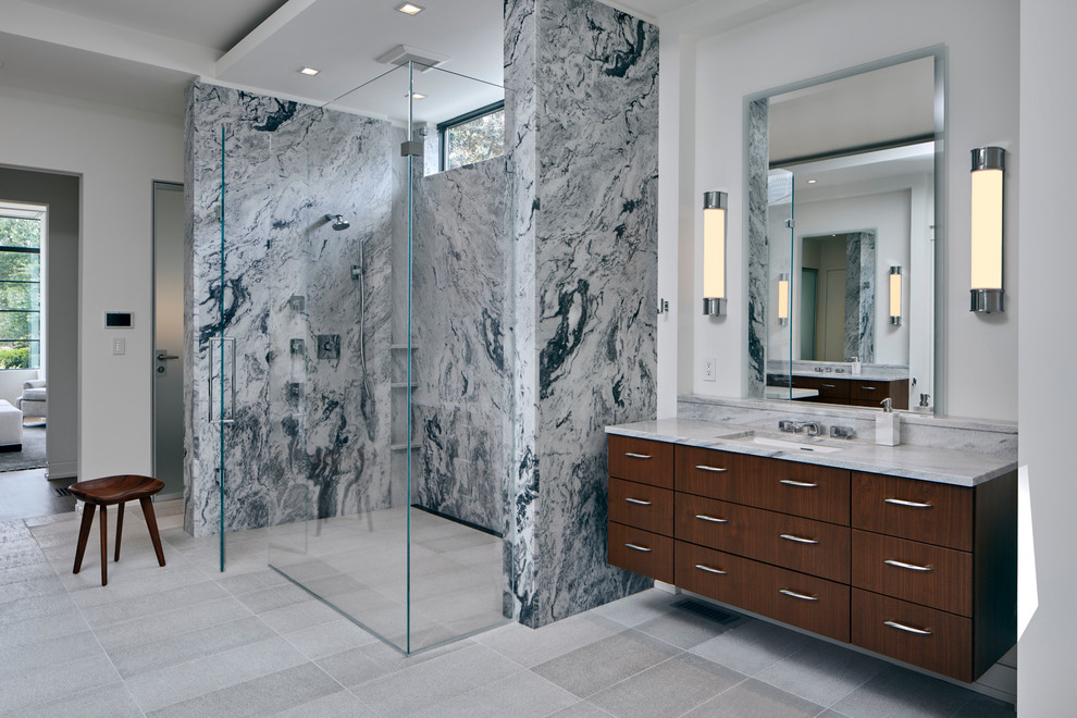 Inredning av ett modernt stort vit vitt badrum, med en kantlös dusch, marmorkakel, vita väggar, kalkstensgolv, ett undermonterad handfat, marmorbänkskiva, dusch med gångjärnsdörr, släta luckor, skåp i mörkt trä, grå kakel och grått golv