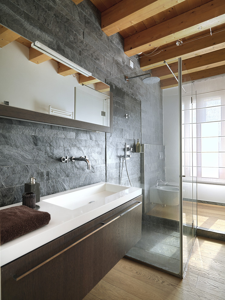 Modernes Badezimmer mit flächenbündigen Schrankfronten, dunklen Holzschränken, Duschnische, Bidet, grauer Wandfarbe, hellem Holzboden, integriertem Waschbecken, Schieferfliesen und Steinwänden in London