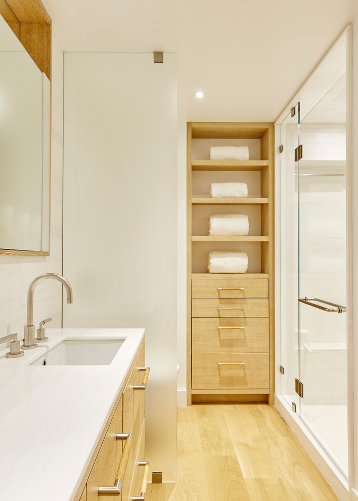Foto på ett mellanstort funkis en-suite badrum, med släta luckor, skåp i slitet trä, en dusch i en alkov, en toalettstol med hel cisternkåpa, vit kakel, marmorkakel, vita väggar, ljust trägolv, ett undermonterad handfat och marmorbänkskiva