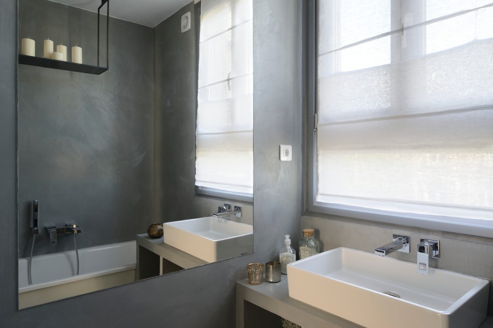 Modelo de cuarto de baño principal contemporáneo pequeño con lavabo tipo consola, encimera de cemento, bañera encastrada, sanitario de pared, suelo de cemento, armarios abiertos, puertas de armario grises y paredes grises