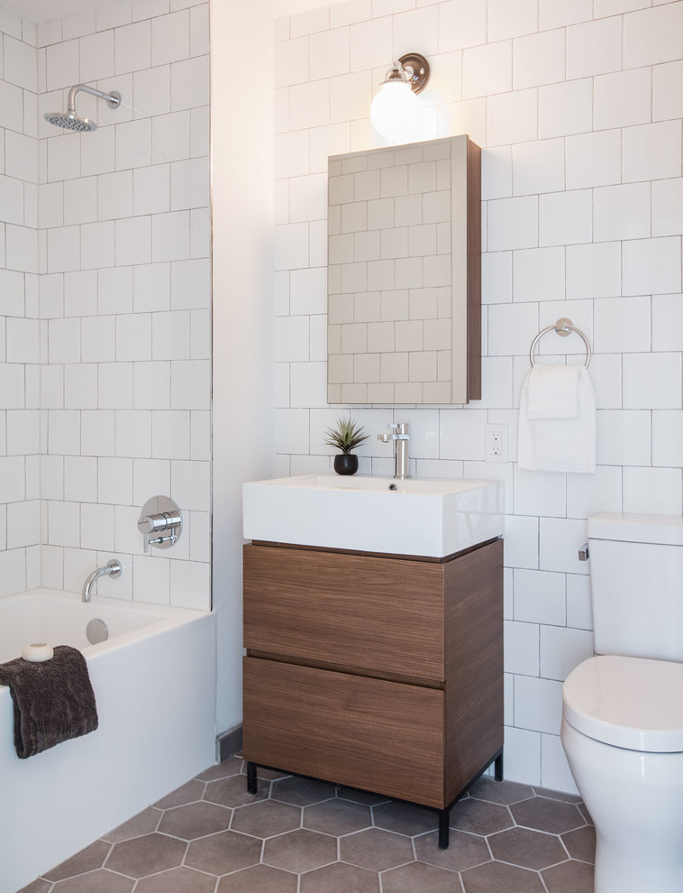 Cette image montre une salle d'eau design en bois brun avec un placard à porte plane, une baignoire d'angle, un combiné douche/baignoire, WC séparés, un carrelage blanc, un mur blanc, un plan vasque et un sol gris.