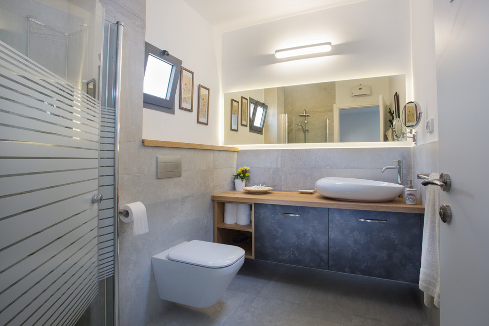Inredning av ett modernt mellanstort en-suite badrum, med svarta skåp, en hörndusch, en vägghängd toalettstol, grå kakel, keramikplattor, vita väggar, klinkergolv i keramik, träbänkskiva, grått golv, dusch med gångjärnsdörr, ett fristående handfat och släta luckor