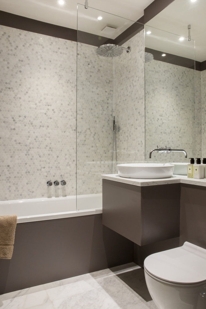 Small contemporary bathroom in London with a built-in bath, a shower/bath combination, a bidet, grey tiles, white tiles, marble tiles, a wall-mounted sink and white floors.