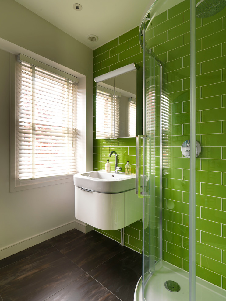 Modern inredning av ett litet badrum för barn, med släta luckor, vita skåp, en hörndusch, en vägghängd toalettstol, grön kakel, glaskakel, vita väggar, klinkergolv i keramik och ett integrerad handfat