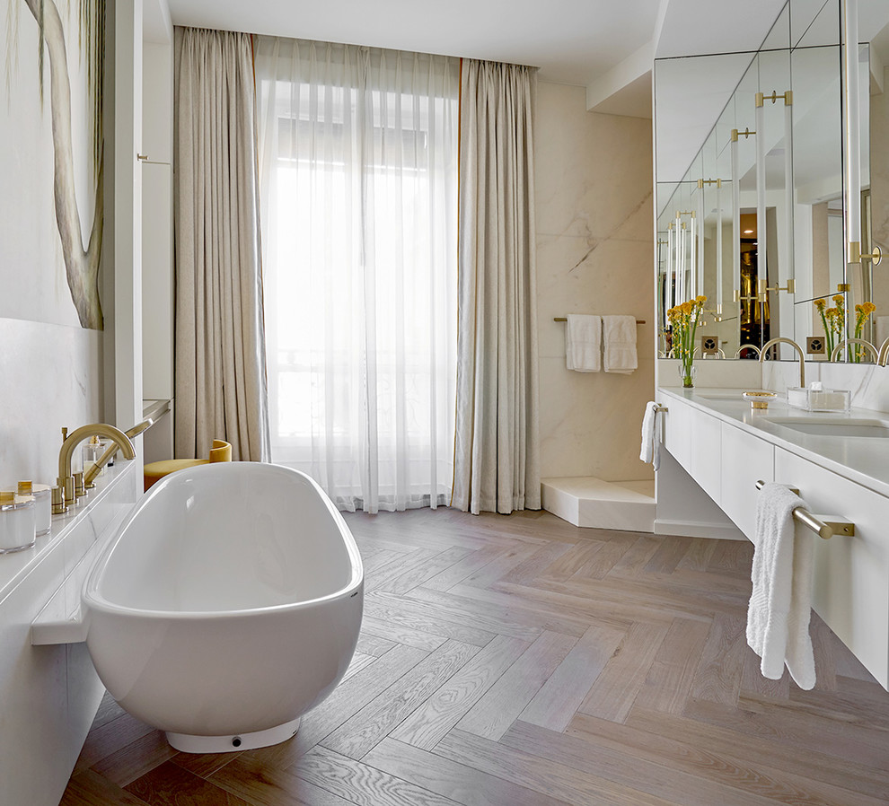 Inredning av ett modernt stort vit vitt en-suite badrum, med släta luckor, vita skåp, ett fristående badkar, en dusch i en alkov, en vägghängd toalettstol, marmorkakel, vita väggar, mellanmörkt trägolv, ett undermonterad handfat, marmorbänkskiva och med dusch som är öppen