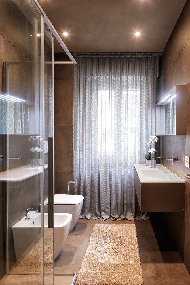 Свежая идея для дизайна: ванная комната в современном стиле с плоскими фасадами, коричневыми фасадами, угловым душем, биде, коричневой плиткой, коричневыми стенами, душевой кабиной, монолитной раковиной, коричневым полом, душем с раздвижными дверями, белой столешницей и зеркалом с подсветкой - отличное фото интерьера