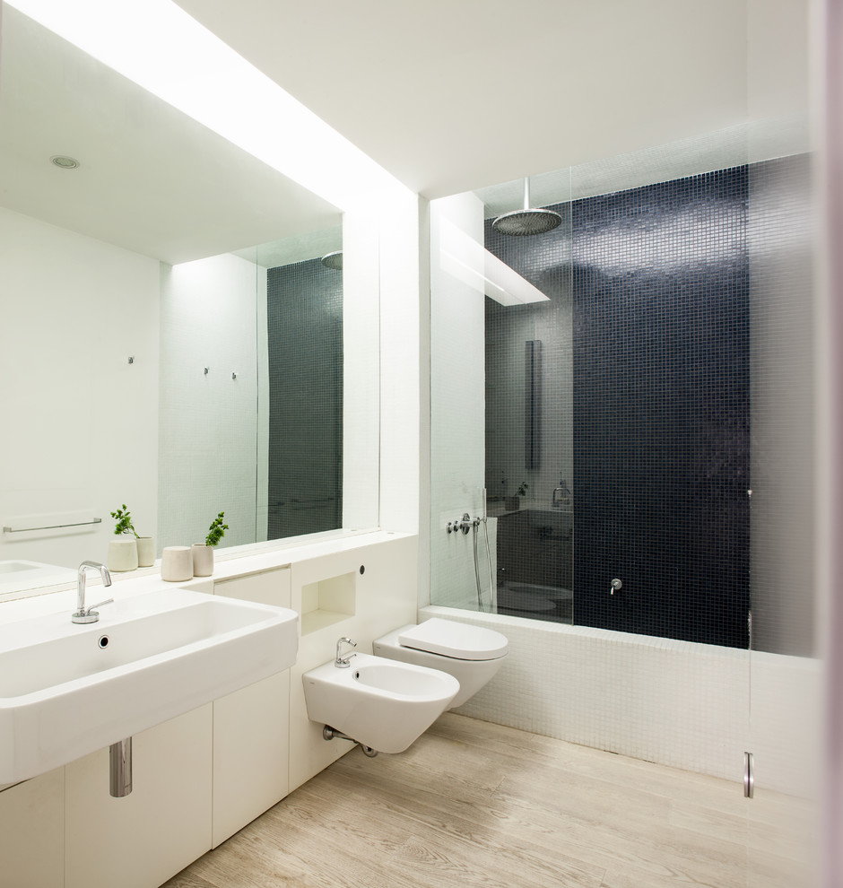 На фото: большая главная ванная комната в скандинавском стиле с подвесной раковиной, плоскими фасадами, белыми фасадами, раздельным унитазом, синей плиткой, белыми стенами, светлым паркетным полом и душем над ванной с