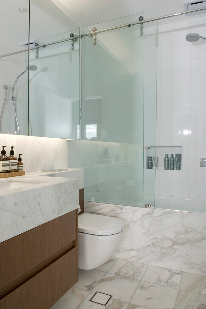 Inspiration for a small modern shower room bathroom in Sydney with a submerged sink, medium wood cabinets, marble worktops, a built-in bath, a shower/bath combination, a one-piece toilet, white tiles, porcelain tiles, white walls, marble flooring and flat-panel cabinets.