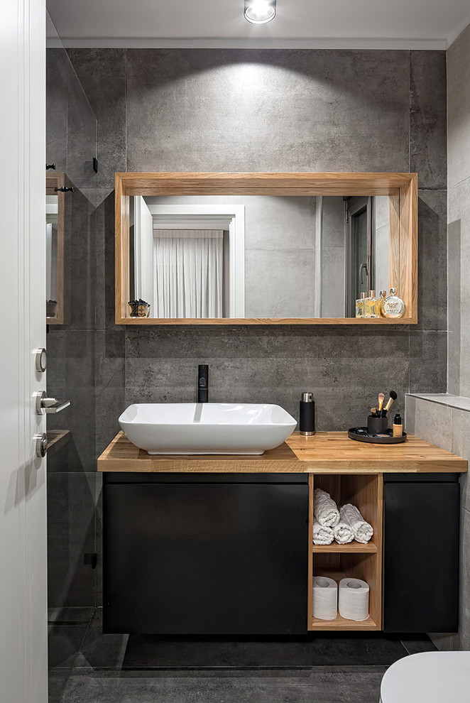 Inspiration pour une petite salle d'eau nordique avec sol en stratifié, un placard à porte plane, des portes de placard noires, un carrelage gris, un mur gris, une vasque, un plan de toilette en bois, un sol gris et un plan de toilette marron.