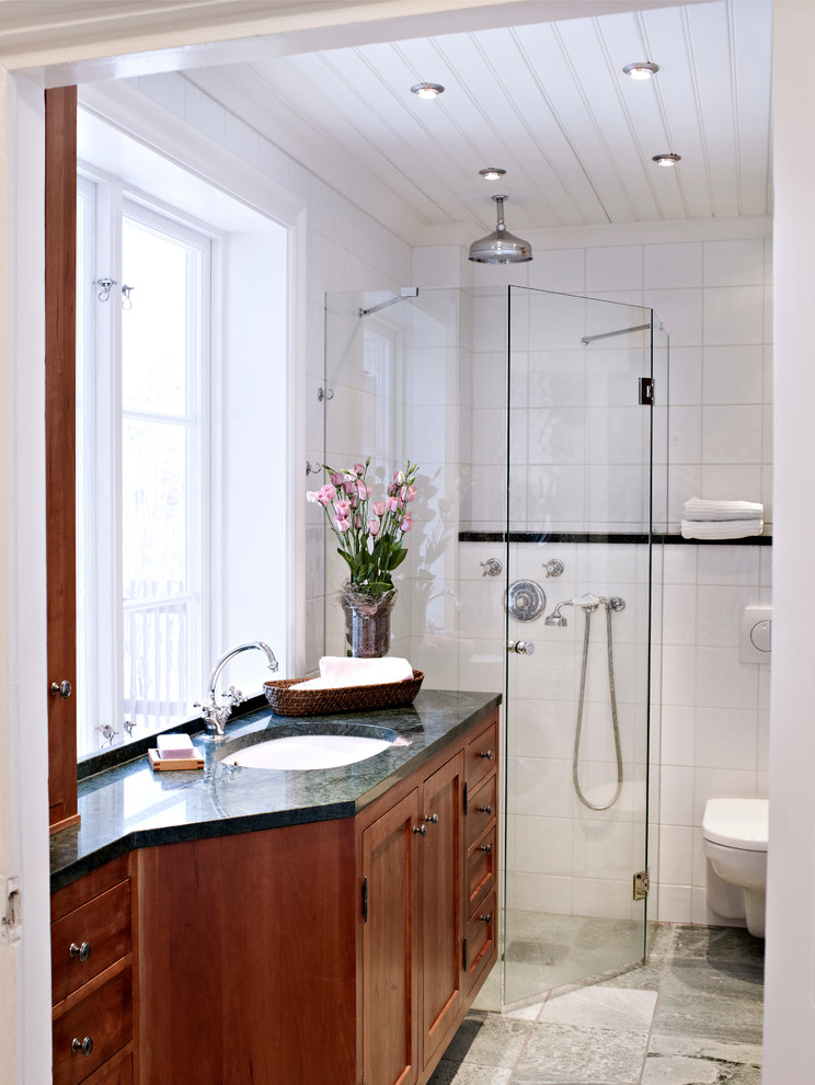 Klassisk inredning av ett mellanstort badrum, med luckor med upphöjd panel, skåp i mellenmörkt trä, en hörndusch, en vägghängd toalettstol, vit kakel, keramikplattor, vita väggar, klinkergolv i keramik, marmorbänkskiva och ett undermonterad handfat