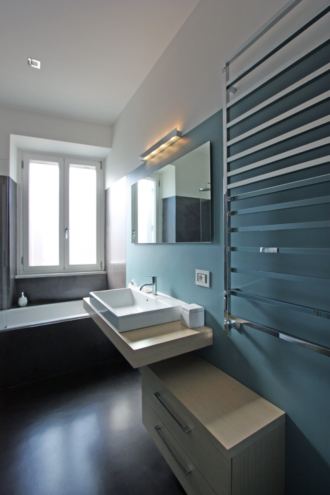 Immagine di una stanza da bagno padronale moderna di medie dimensioni con lavabo a consolle, consolle stile comò, ante in legno chiaro, vasca da incasso, doccia ad angolo, WC sospeso, pareti blu e pavimento in cemento