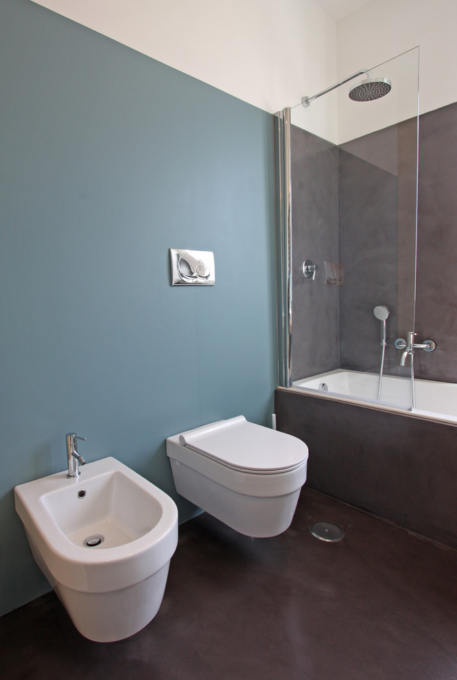 ローマにあるお手頃価格の中くらいなモダンスタイルのおしゃれなマスターバスルーム (コンソール型シンク、家具調キャビネット、淡色木目調キャビネット、ドロップイン型浴槽、コーナー設置型シャワー、壁掛け式トイレ、青い壁、コンクリートの床) の写真