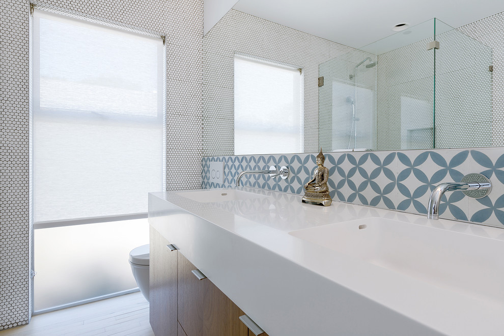 Inspiration pour une salle de bain principale nordique en bois foncé avec un lavabo intégré, un placard à porte plane, un plan de toilette en surface solide, WC suspendus, un carrelage bleu, des carreaux de béton, un mur blanc et parquet clair.