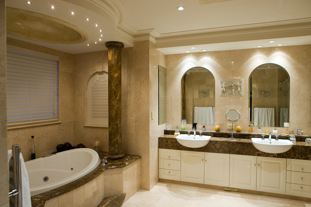 На фото: большая главная ванная комната в средиземноморском стиле с бежевыми фасадами, накладной ванной, двойным душем, унитазом-моноблоком, бежевой плиткой, керамической плиткой, бежевыми стенами, полом из травертина, настольной раковиной, столешницей из гранита, бежевым полом, душем с распашными дверями, коричневой столешницей, тумбой под две раковины, встроенной тумбой и многоуровневым потолком