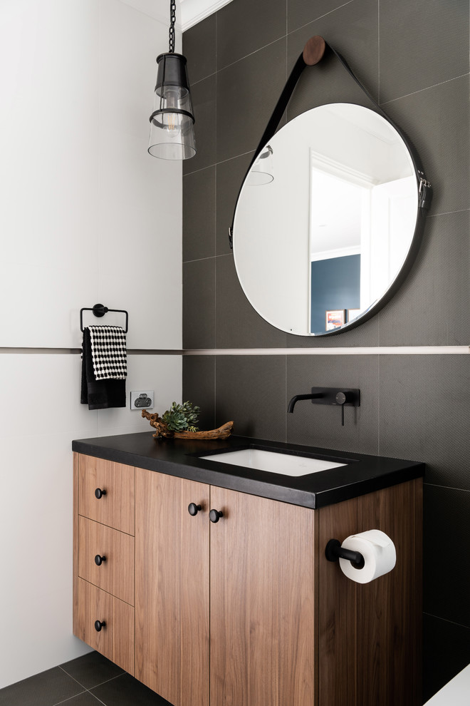 Modernes Badezimmer mit flächenbündigen Schrankfronten, hellbraunen Holzschränken, schwarzen Fliesen, schwarzer Wandfarbe, Unterbauwaschbecken, schwarzem Boden und schwarzer Waschtischplatte in Perth