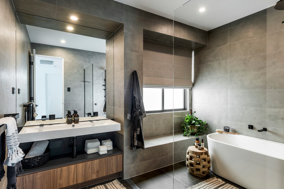 Idéer för funkis en-suite badrum, med släta luckor, skåp i mellenmörkt trä, ett fristående badkar, en kantlös dusch, grå kakel, grå väggar, ett väggmonterat handfat, grått golv och med dusch som är öppen