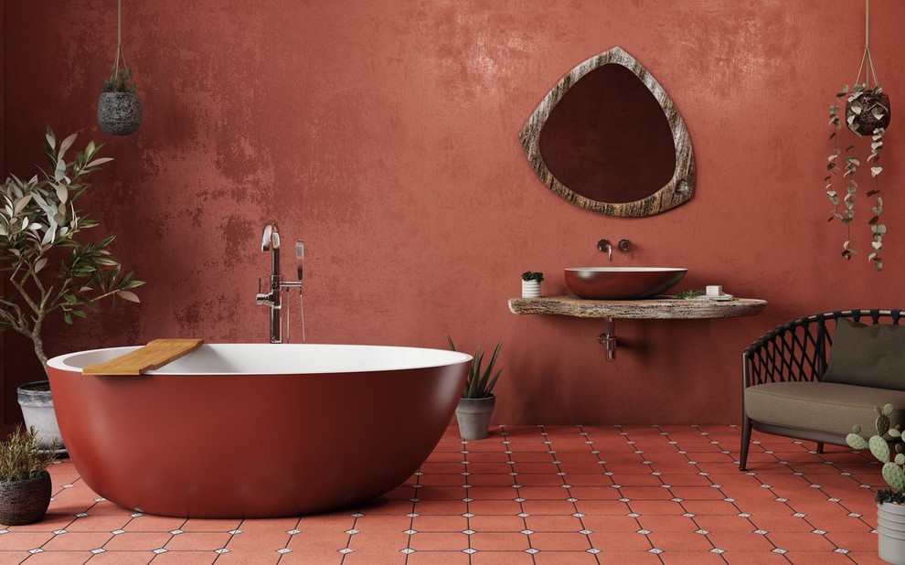 Cette image montre une grande salle de bain principale méditerranéenne avec un placard sans porte, une baignoire indépendante, un mur rouge, une vasque, un plan de toilette en bois et un sol rouge.