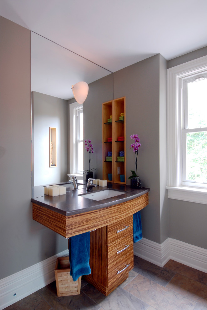 Inredning av ett modernt mellanstort brun brunt badrum, med öppna hyllor, skåp i mellenmörkt trä, ett hörnbadkar, en toalettstol med hel cisternkåpa, grå väggar, klinkergolv i porslin, ett undermonterad handfat, bänkskiva i akrylsten och flerfärgat golv
