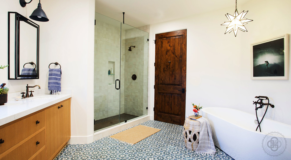 Пример оригинального дизайна: большая главная ванная комната в средиземноморском стиле с фасадами островного типа, фасадами цвета дерева среднего тона, отдельно стоящей ванной, душем в нише, раздельным унитазом, желтой плиткой, терракотовой плиткой, белыми стенами, полом из цементной плитки, врезной раковиной, столешницей из искусственного кварца, синим полом, душем с распашными дверями и белой столешницей