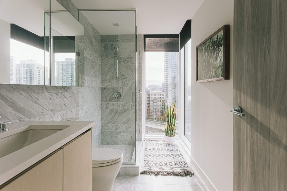 На фото: ванная комната в современном стиле с плоскими фасадами, светлыми деревянными фасадами, угловым душем, серой плиткой, серыми стенами, врезной раковиной, серым полом, душем с распашными дверями и бежевой столешницей