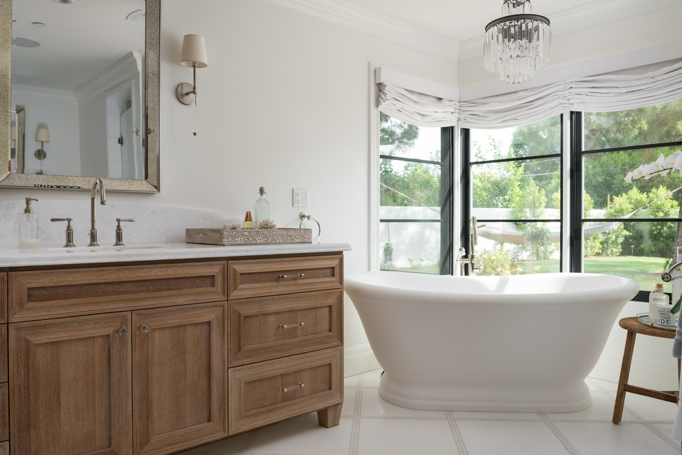 Inredning av ett klassiskt stort vit vitt en-suite badrum, med skåp i mellenmörkt trä, ett fristående badkar, vit kakel, marmorgolv, marmorbänkskiva, vitt golv och luckor med infälld panel