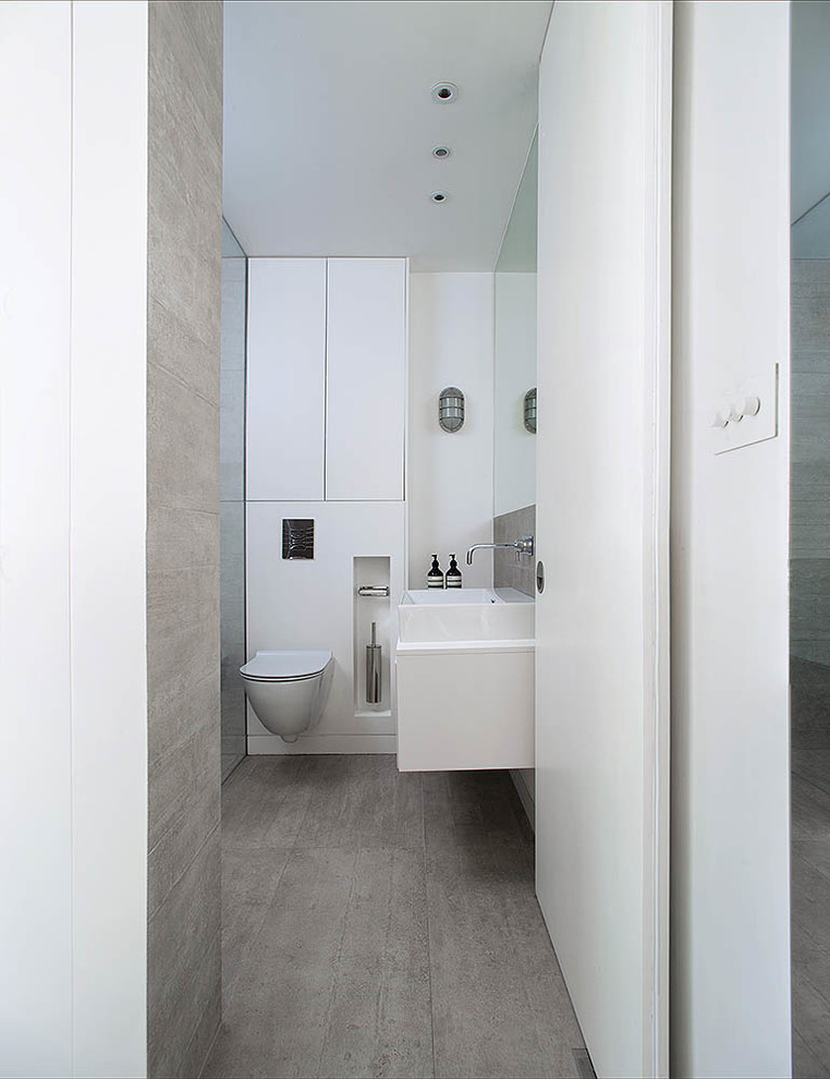 Exemple d'une petite salle de bain tendance avec un plan vasque, un placard à porte plane, des portes de placard blanches, une douche ouverte, WC suspendus, un carrelage gris, des carreaux de porcelaine, un mur gris et un sol en carrelage de porcelaine.